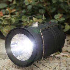 Złożona lampa Retoo leżąca na kamieniu, świecąca reflektorem latarki w kierunku zieleni