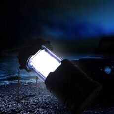 Świecąca lampa kempingowa trzymana w dłoni w rękawicy, nocą przed terenowym samochodem