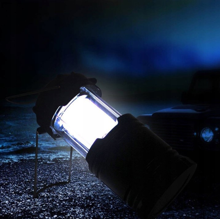 Lampa kempingowa Retoo – oświetlenie nocne przy samochodzie Świecąca lampa kempingowa trzymana w dłoni w rękawicy, nocą przed terenowym samochodem